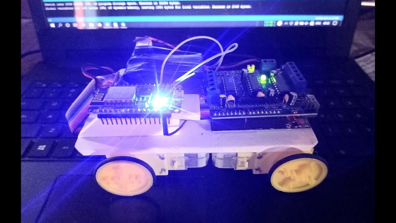 The car sitting on a laptop keyboard: an ESP8266 board and a motor driver bolted to a small four-wheel chassis, status LEDs lit.
